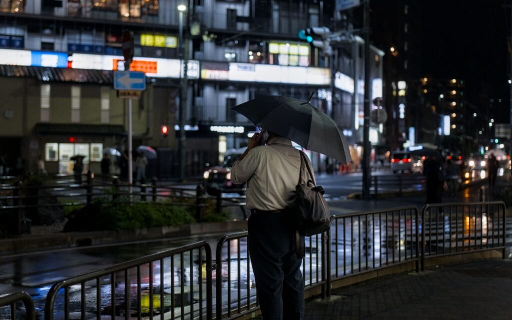 A man with an umbrella walks through rain-soaked streets of Kyoto at night.